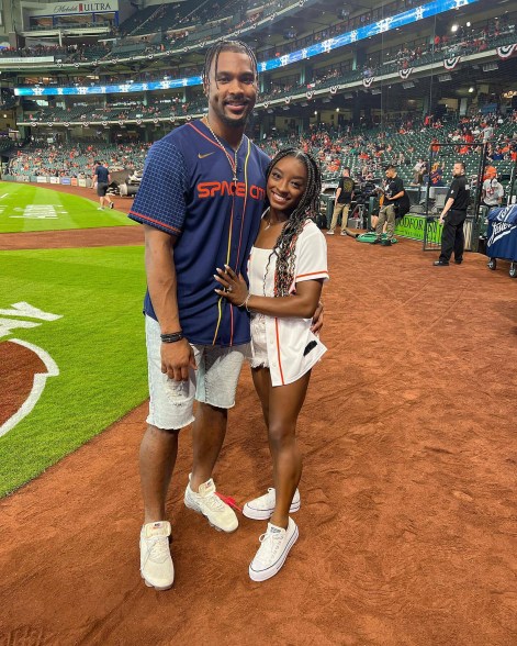 Simone Biles and Jonathan Owens stand on a baseball field