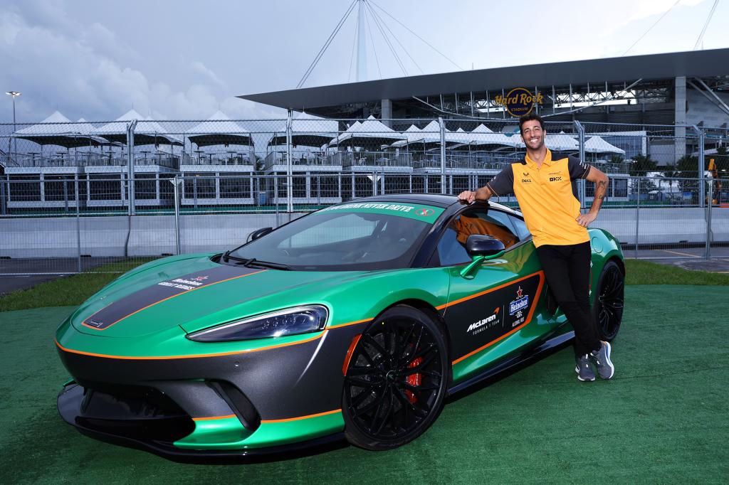 Daniel Ricciardo standing next to a sports car.