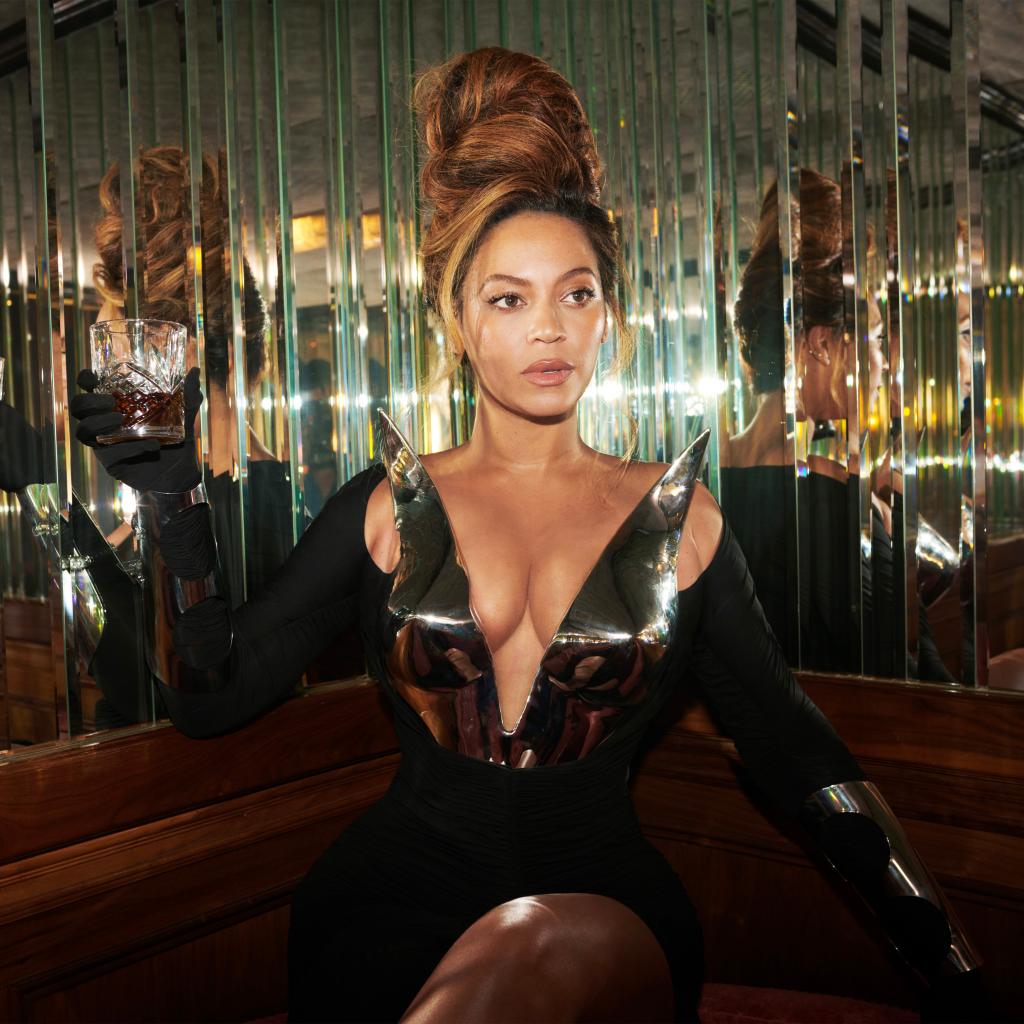 Beyoncé sitting in front of a mirror wall while holding a cocktail.