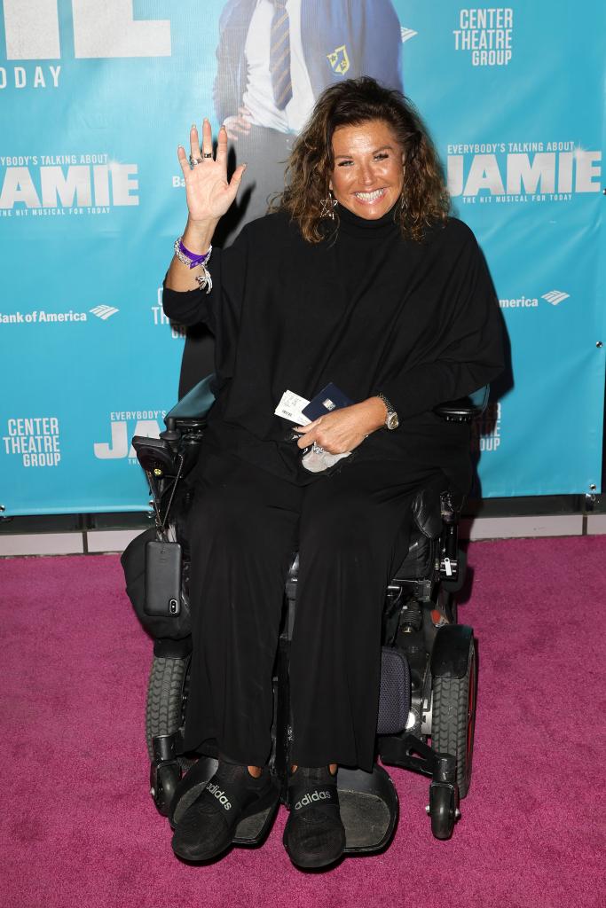 Abby Lee Miller sitting in a wheelchair on a red carpet.