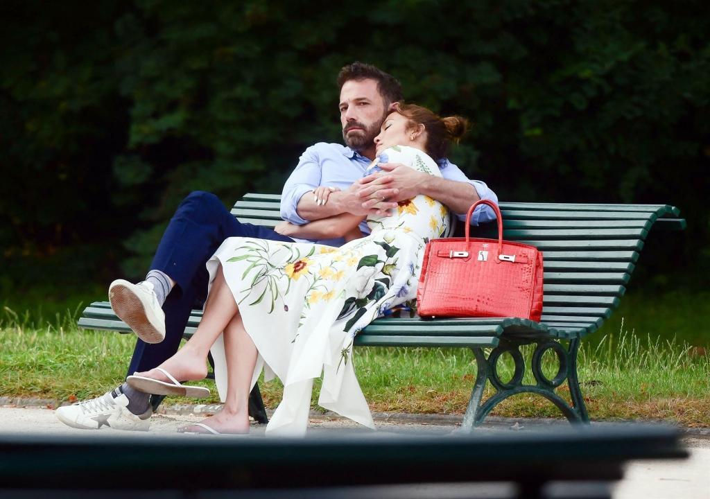 Ben Affleck and Jennifer Lopez snuggling on a park bench.