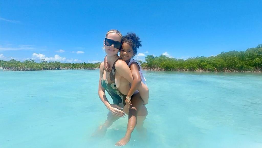 Khloé Kardashian holding daughter True on her back in the ocean.