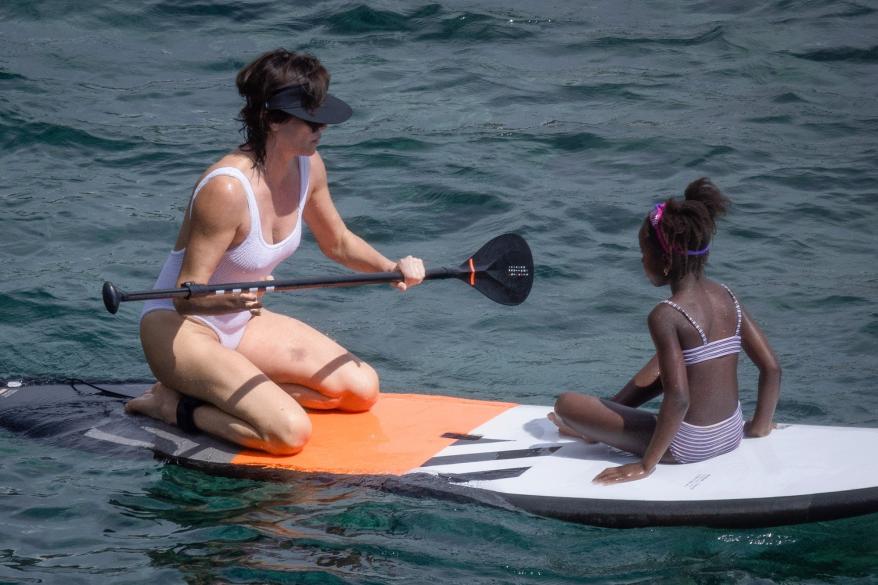 Charlize Theron and her daughter sit on a surfboard off the coast of Porto Ercole