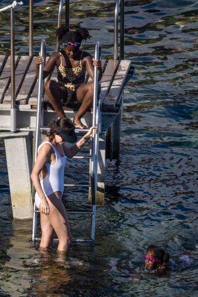 Charlize Theron and her older daughter using a ladder on the end of a dock to go into the water while her younger daughter treads water nearby