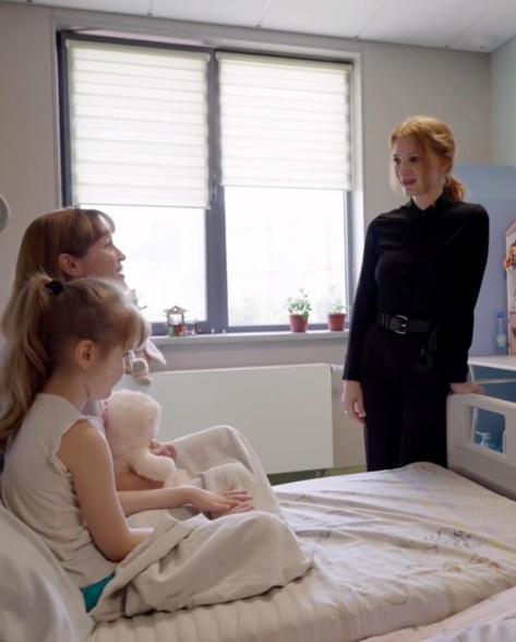 Jessica Chastain bedside talking to a child who is staying at the hospital and an adult next to the child