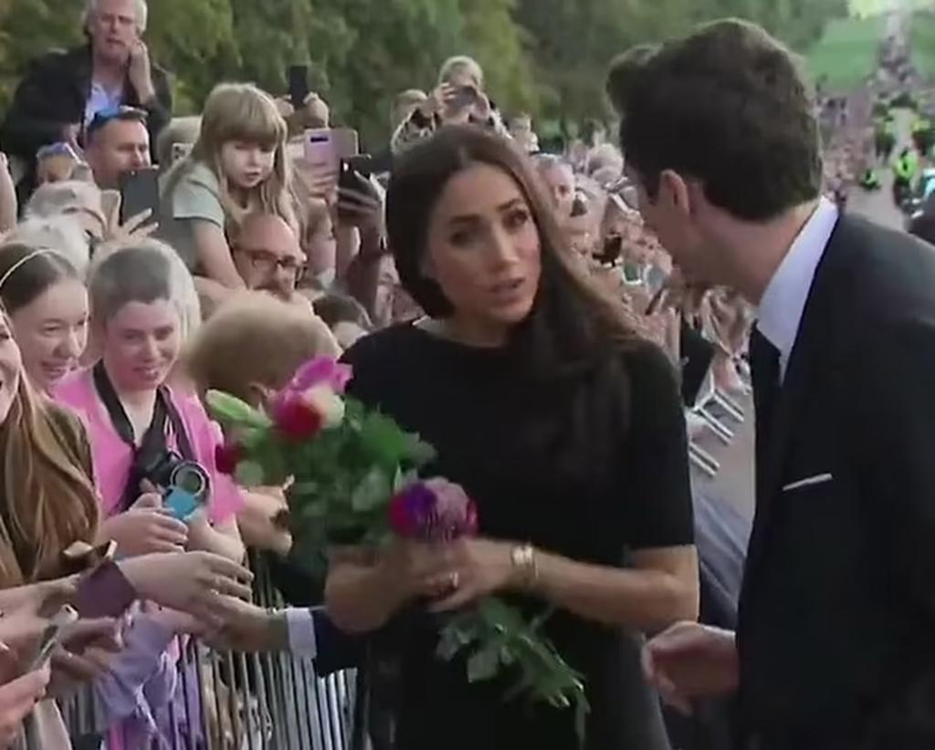 Meghan Markle talking to a royal aide with flowers in her hand.