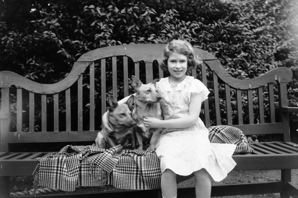 Princess Elizabeth sitting on a garden seat with two corgi dogs at her home on 145 Piccadilly, London in 1936.