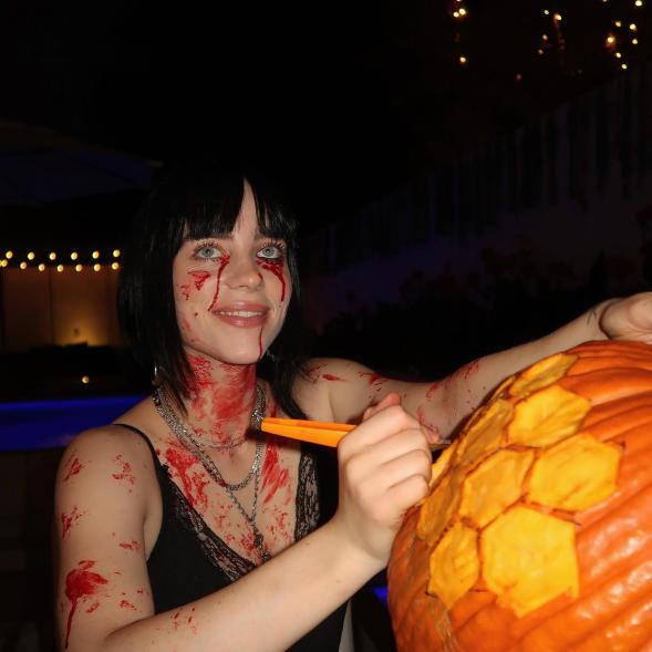 Billie Eilish carving a pumpkin while covered in fake blood.