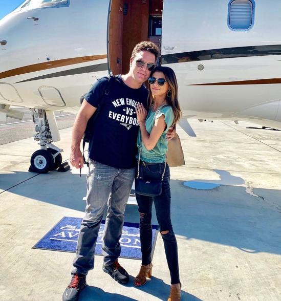 Dane Cook and Kelsi Taylor posing in front of a private jet.