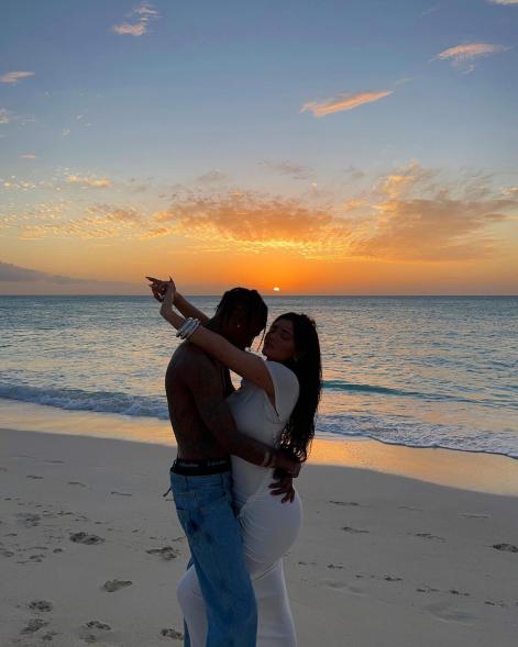 Kylie Jenner and Travis Scott hugging on a beach at sunset.