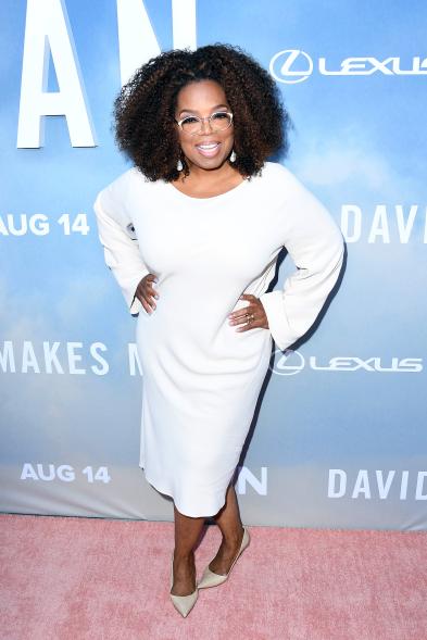 Oprah in a white dress posing with her hands on her hips on the red carpet