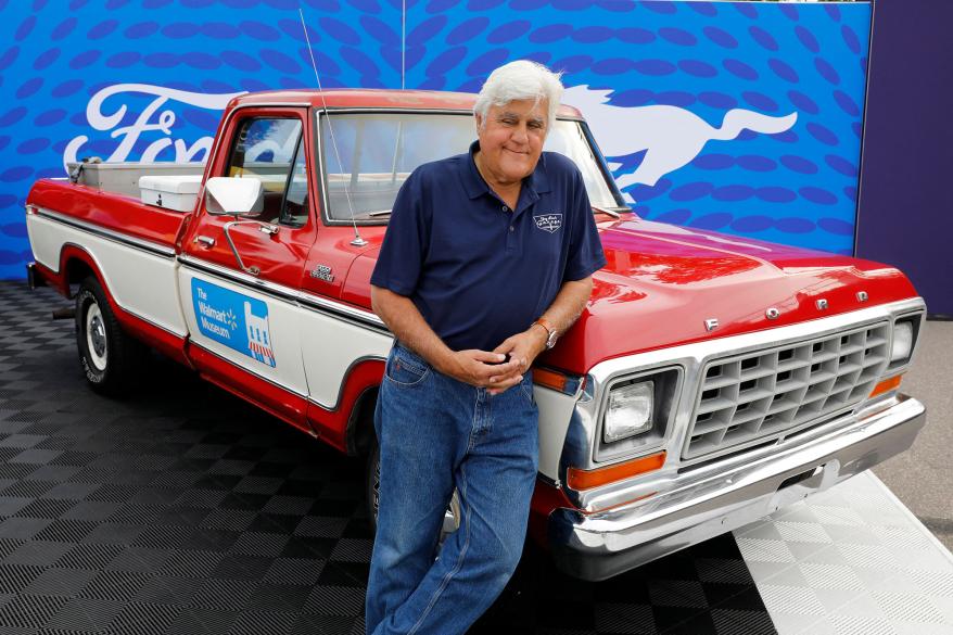 Jay Leno leaning against a classic car.