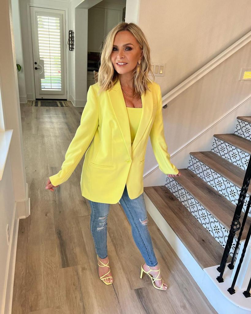 Tamra Judge poses at foot of stairs in yellow blazer, jeans and heels