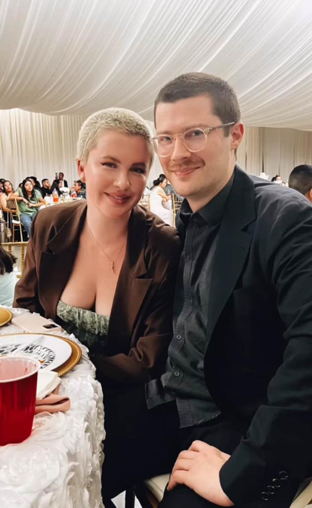 Ireland Baldwin and RAC sitting and smiling together.