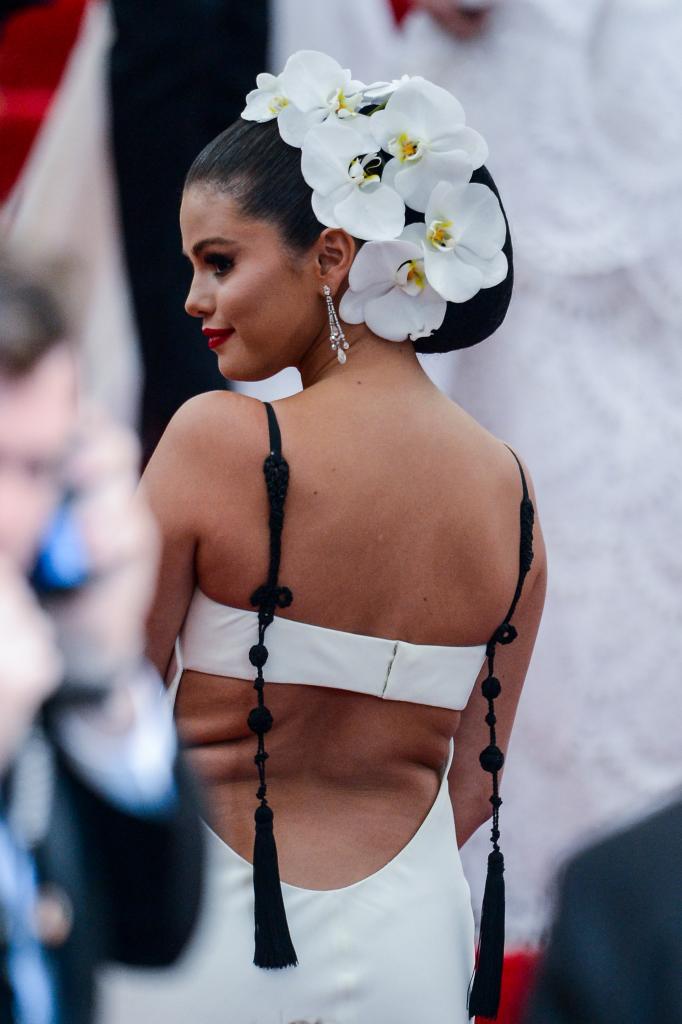 Selena Gomez in white dress from behind with flower hair accent piece