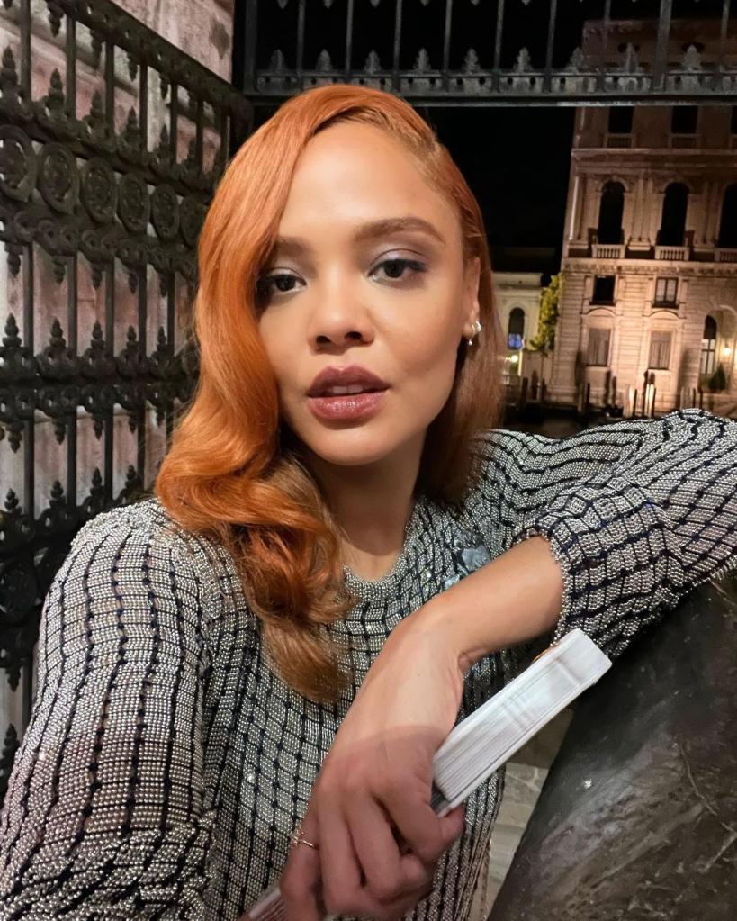 Tessa Thompson wearing a gray sweater with red hair in a selfie.