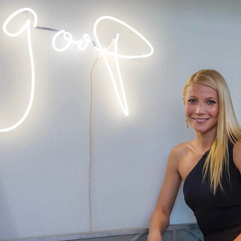 Gwyneth Paltrow smiles beside Goop sign
