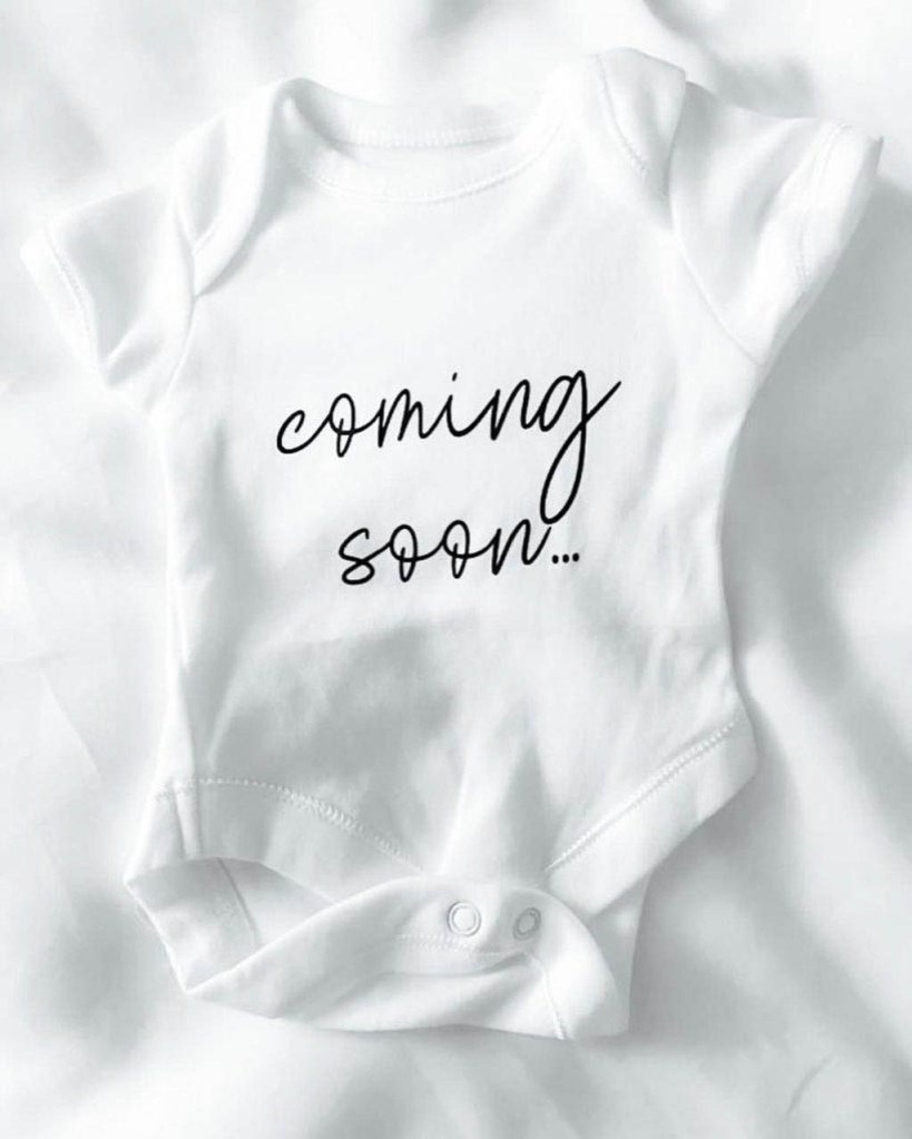 A white onesie that reads "coming soon..."
