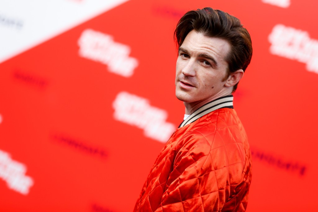 Drake Bell on a red carpet wearing a red jacket.