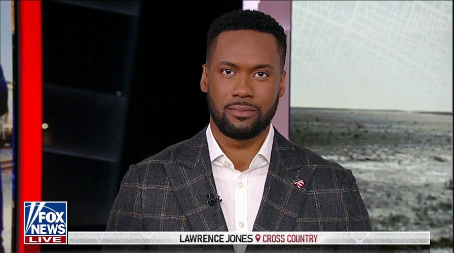 A screenshot of Lawrence Jones, wearing a plaid suit, on the set of his Fox News show "Lawrence Jones Cross Country".