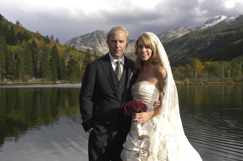 Kevin Costner and Christine Baumgartner in wedding clothing with lake, mountains in background