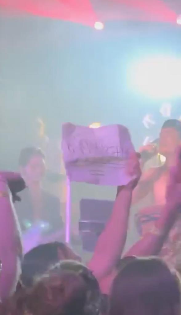 Fan holding up "team Ariana" sign at concert with Tom Sandavol in background