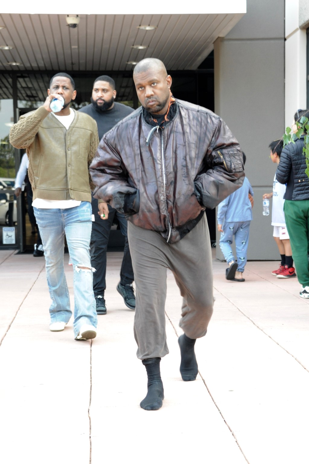 Kanye West walking in a brown leather jacket.