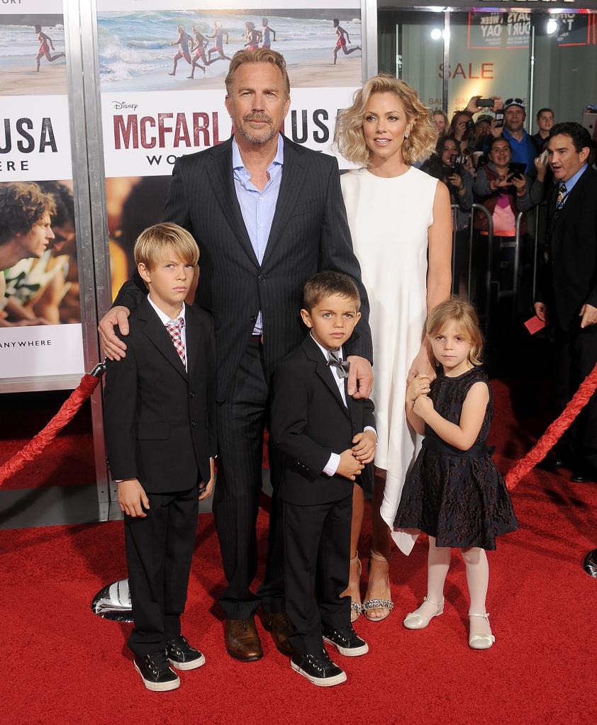 Christine Baumgartner and Kevin Costner posing with their kids when they were younger on a red carpet.