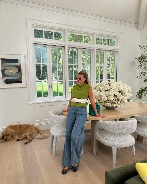 sofia richie leaning against a kitchen table with a dog next to her