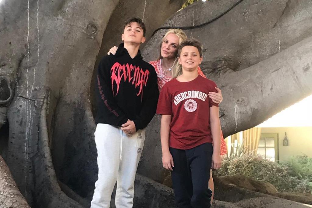 Britney Spears posing with her sons in front of a tree.