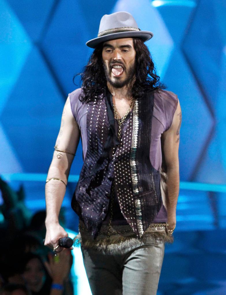 Russell Brand walking with his tongue out.