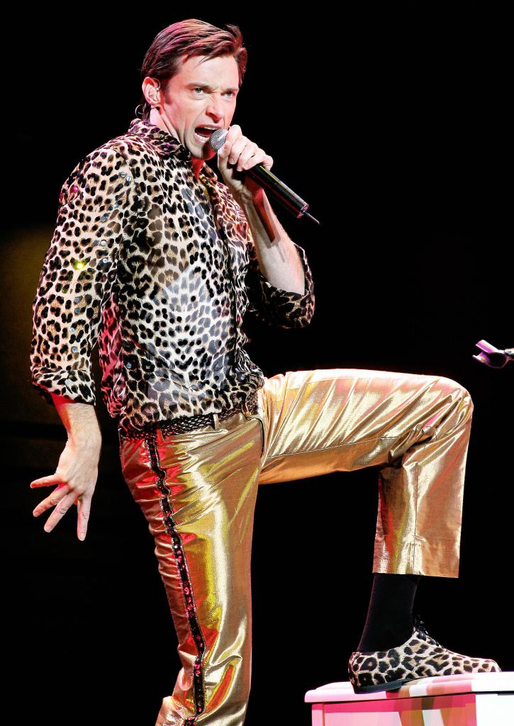 Hugh Jackman dancing in gold pants and a leopard-print shirt.