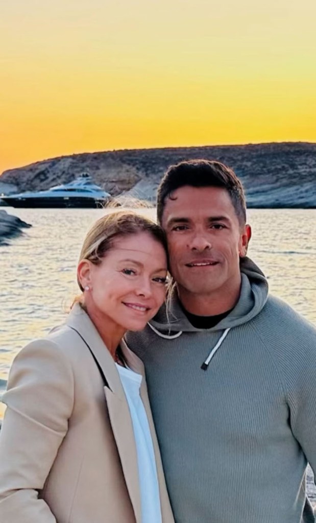 Kelly Ripa and Mark Consuelos smile in front of the water at sunset.