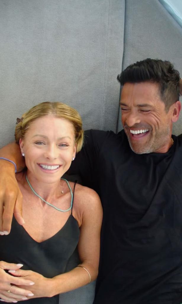 Kelly Ripa in a black dress and Mark Consuelos in a black shirt lie down together and smile.