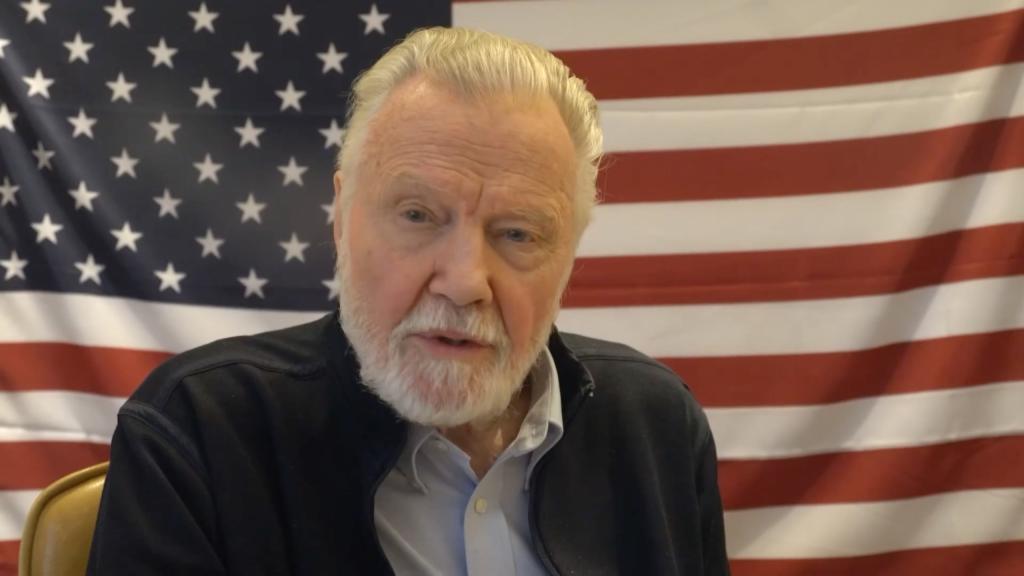 jon voight sitting in front of an american flag