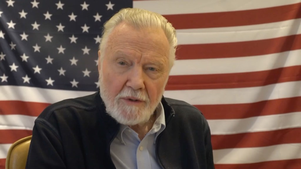 jon voight sitting in front of an american flag