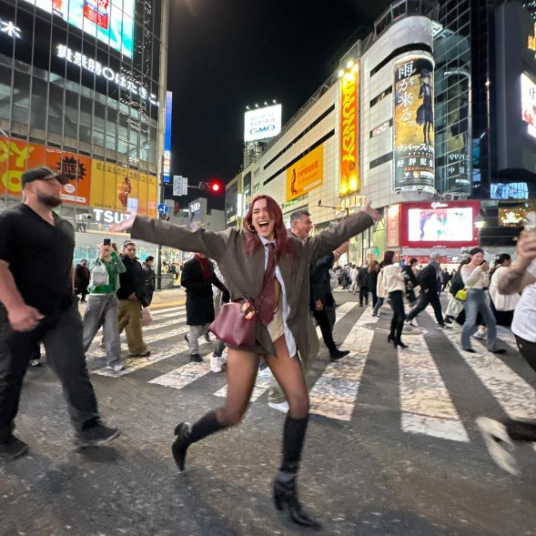 Dua Lipa crossing the street in tokyo with her arms stretched wide