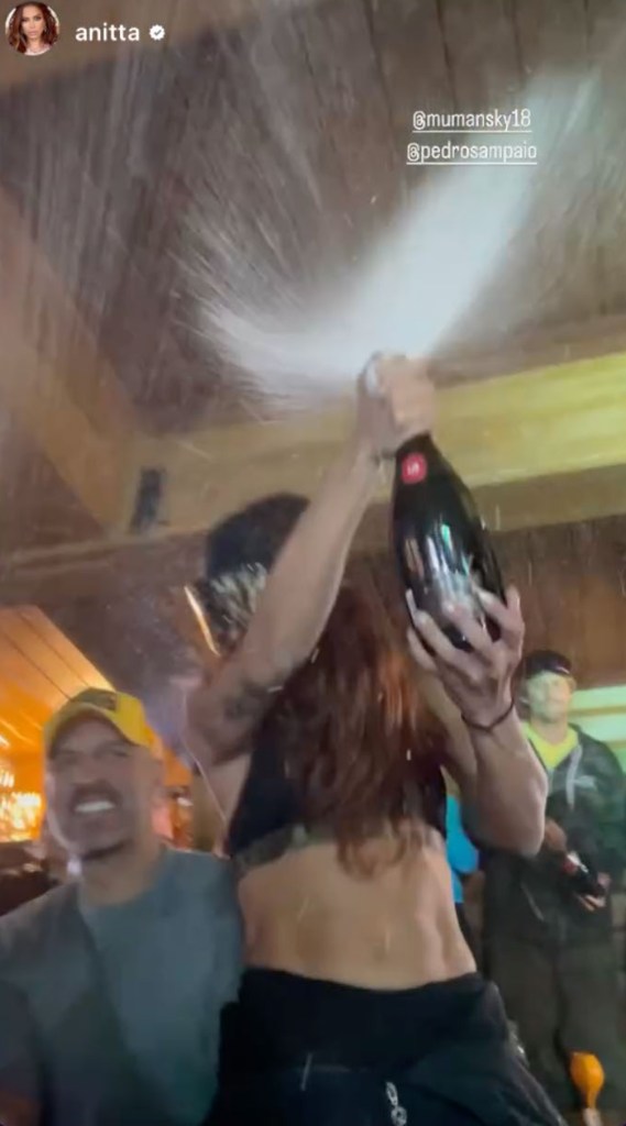 mauricio umansky standing behind anitta who is spraying champagne