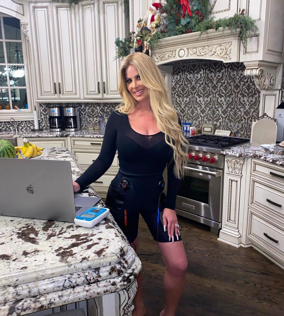 kim zolciak standing in her kitchen with her hand on a laptop