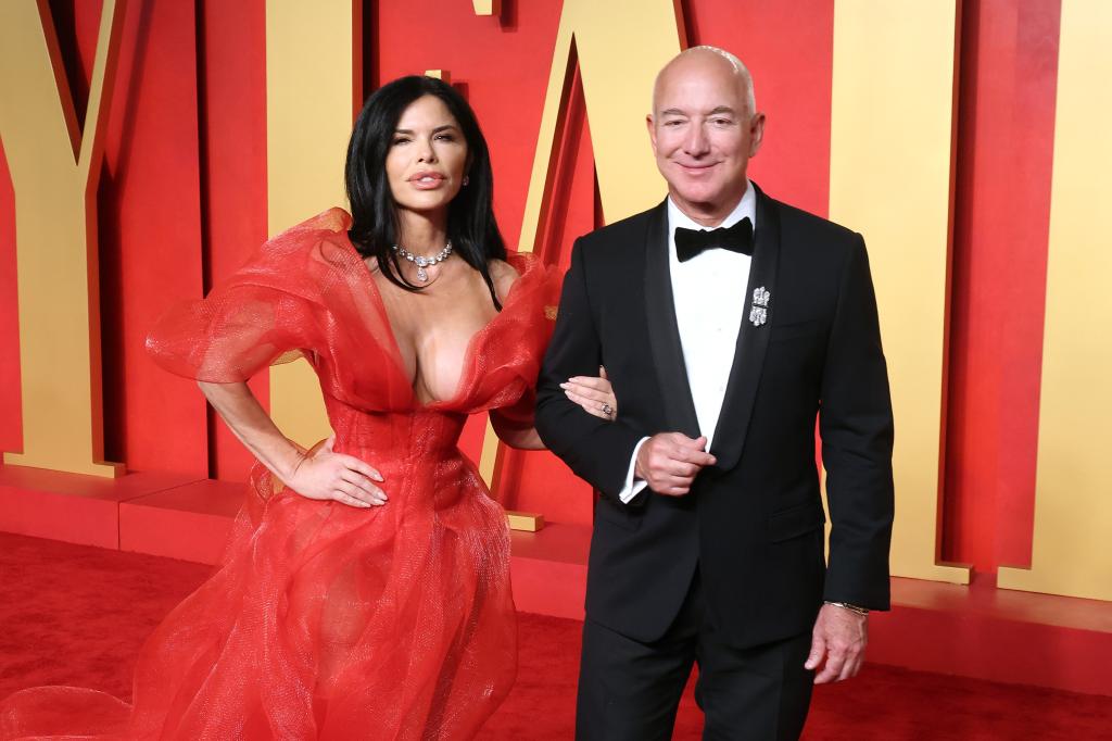 Lauren Sanchez, in red dress, links arms with Jeff Bezos, in a tuxedo.