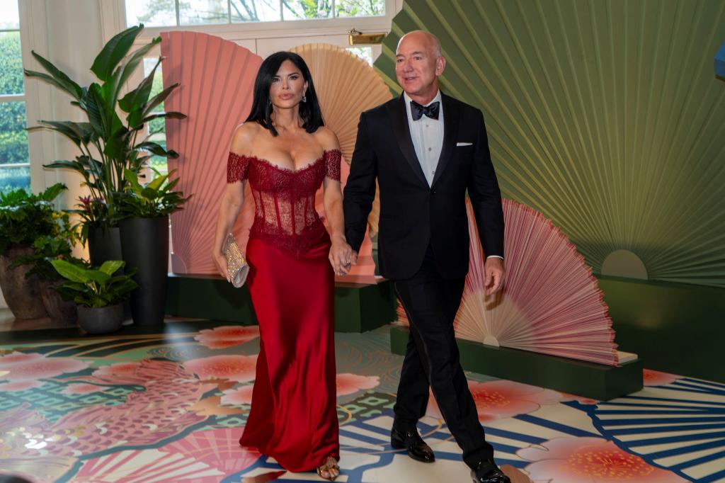 Lauren Sanchez, in red gown, holds hands with Jeff Bezos.