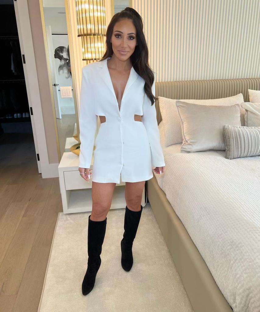 Melissa Gorga posing in a white dress and black boots.