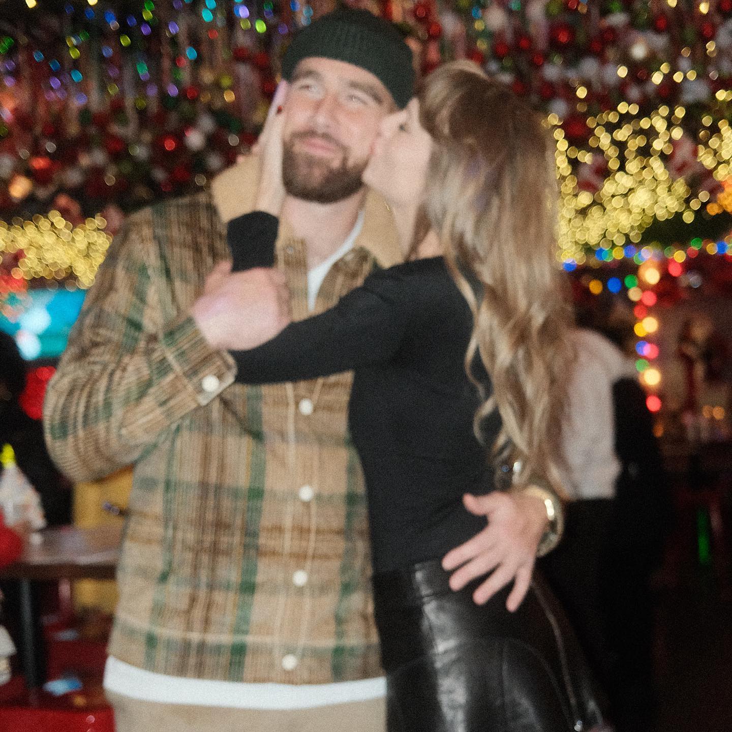 Taylor Swift kissing Travis Kelce on the cheek at a party.