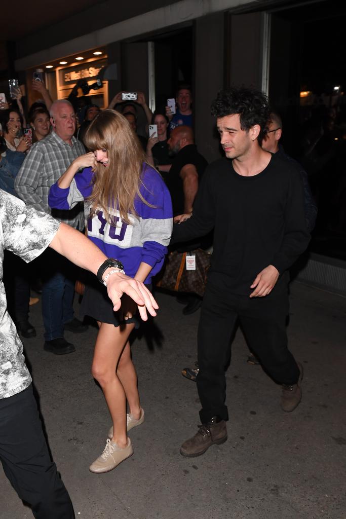 Taylor Swift and Matty Healy walking through a crowd at night