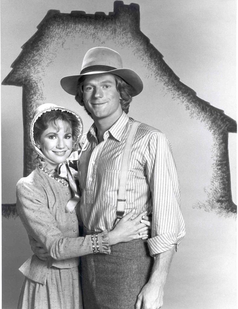 Melissa Gilbert and Dean Butler in period costumes, standing in front of a "Little House" outline. 