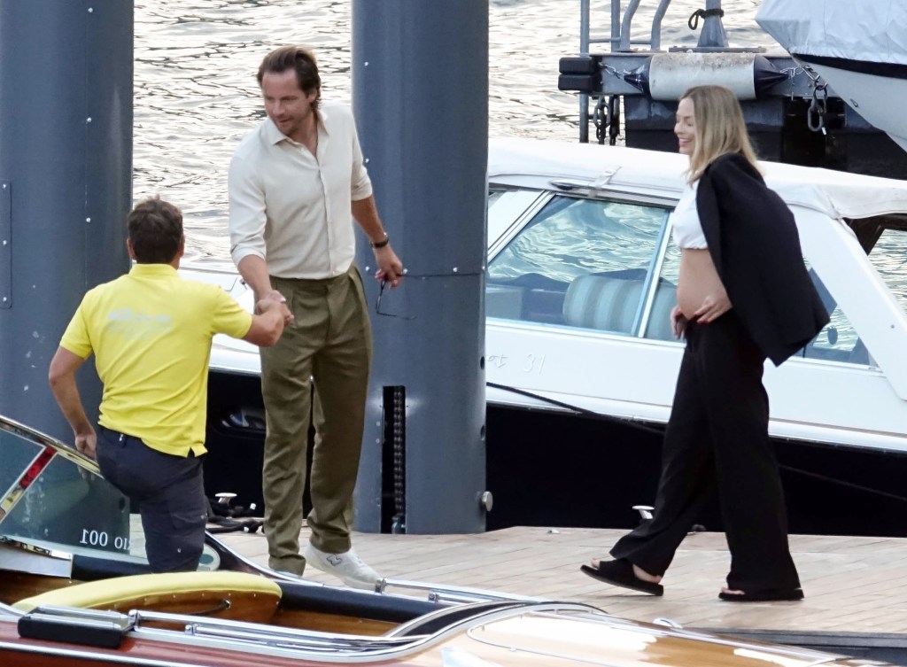 pregnant margot robbie walking toward a boat where her husband is shaking the hands of the captain