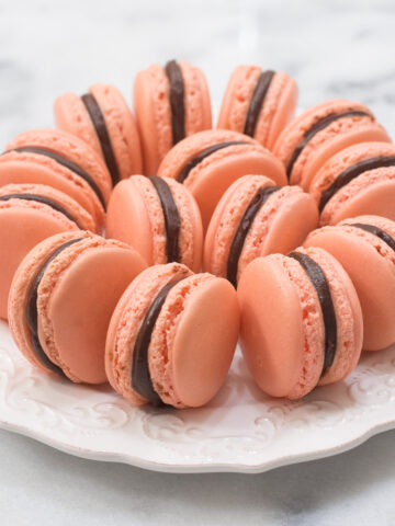 Pink macarons filled with chocolate and raspery on a white plate.