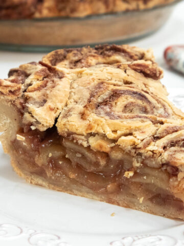 Cinnamon Bun Apple Pie slice on a plate with the pie plate in the background.