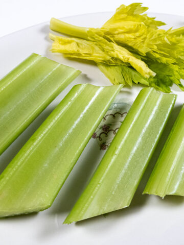 4 pieces of celery with celery leaves on a plate.