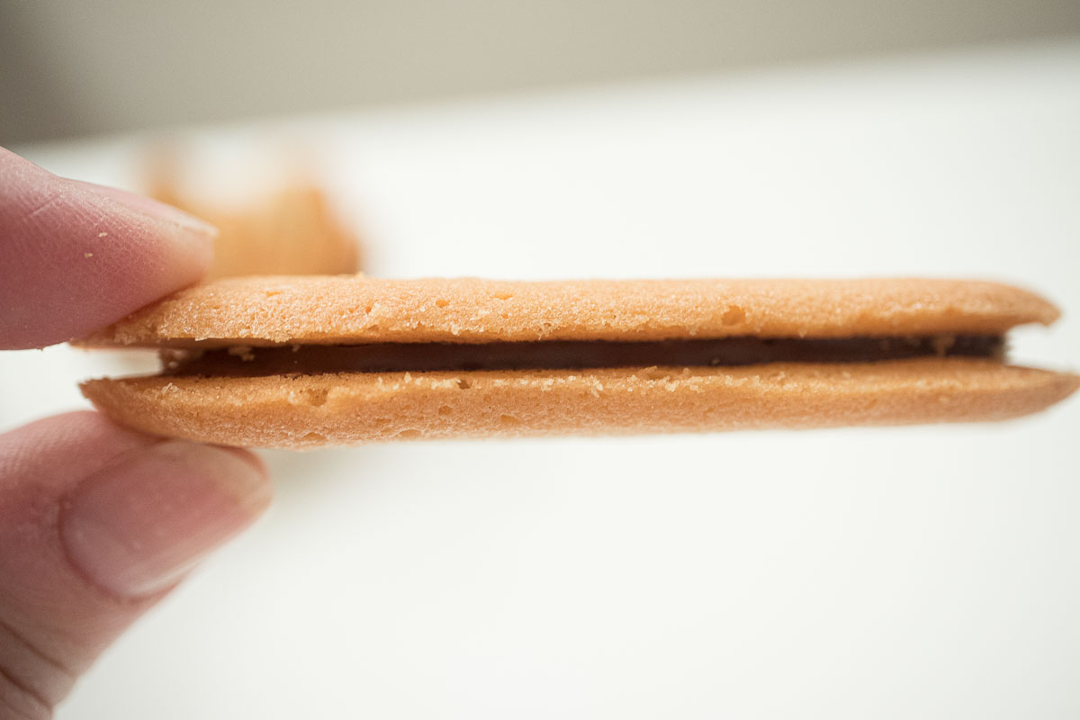 The picture shows a hand holding a chocolate sandwiched cookie so the filling shows.